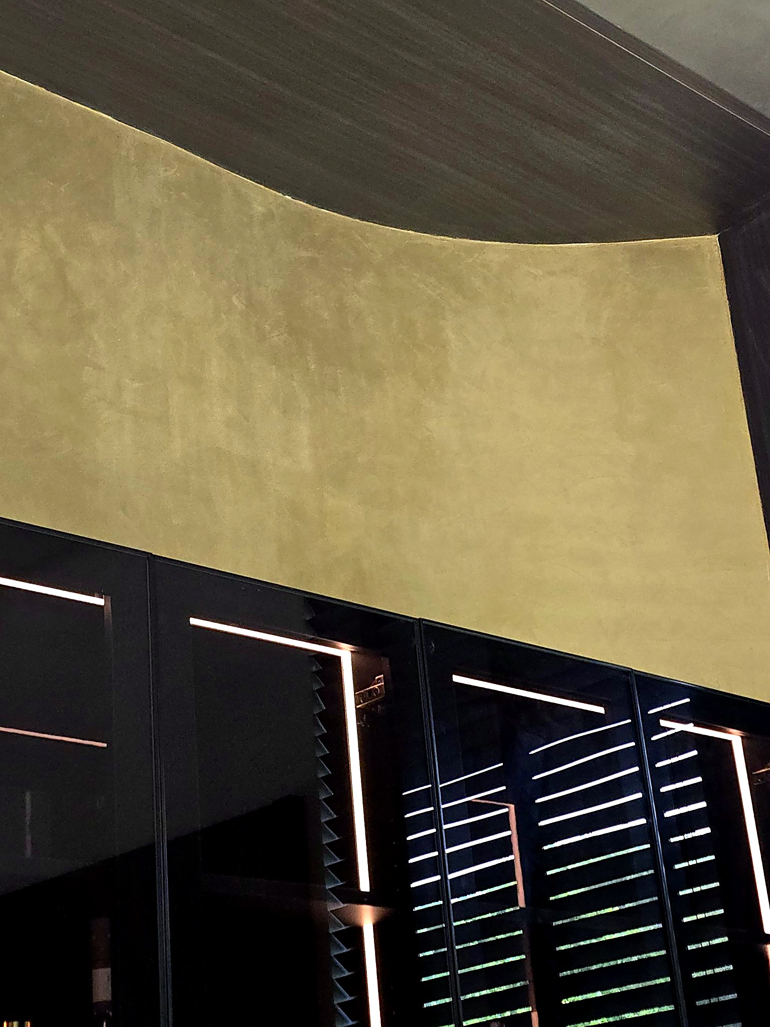 Close detail of curved golden metallic plaster above illuminated bar cabinets
