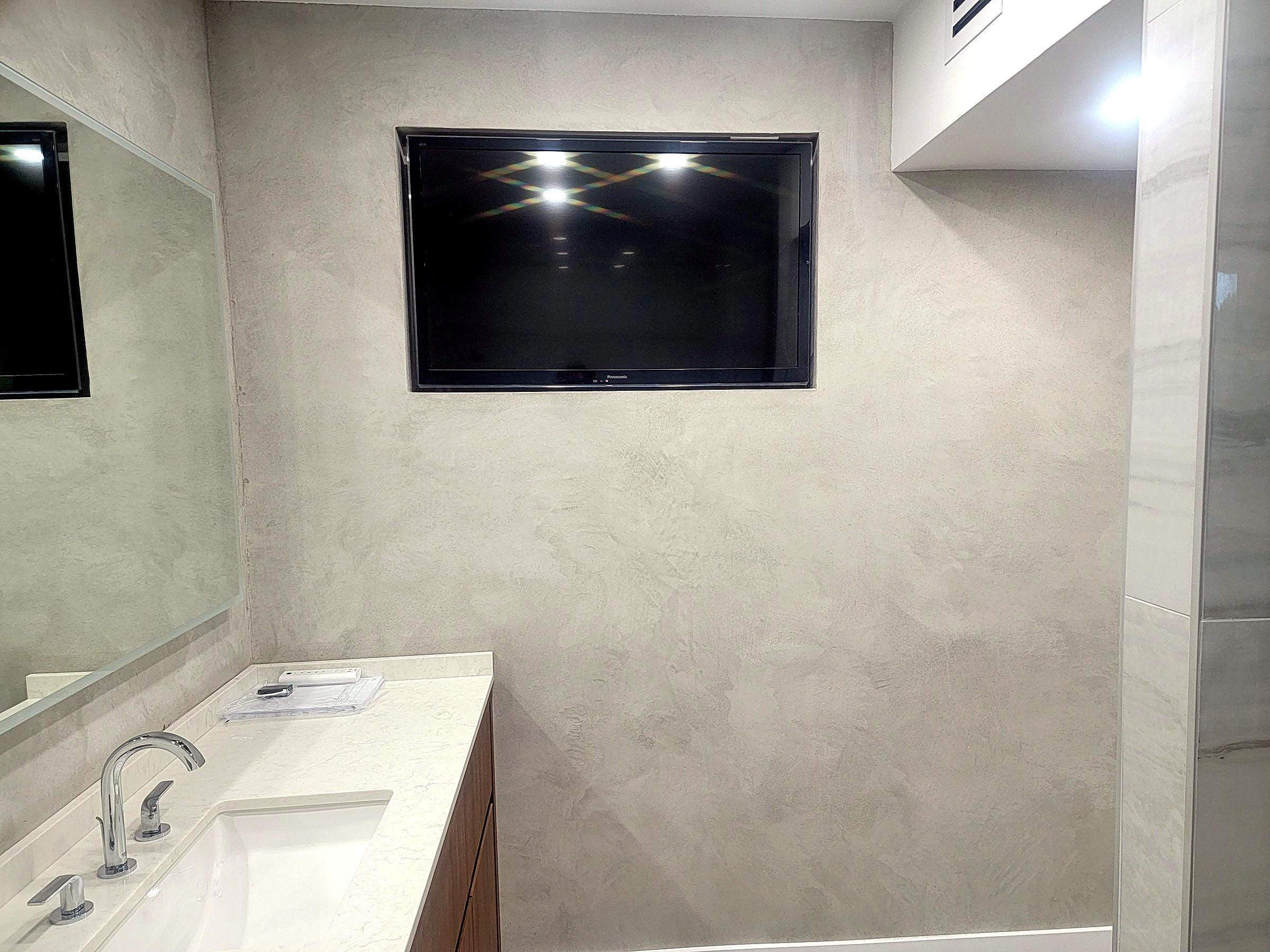 Gray microcement bathroom with a wall-mounted television